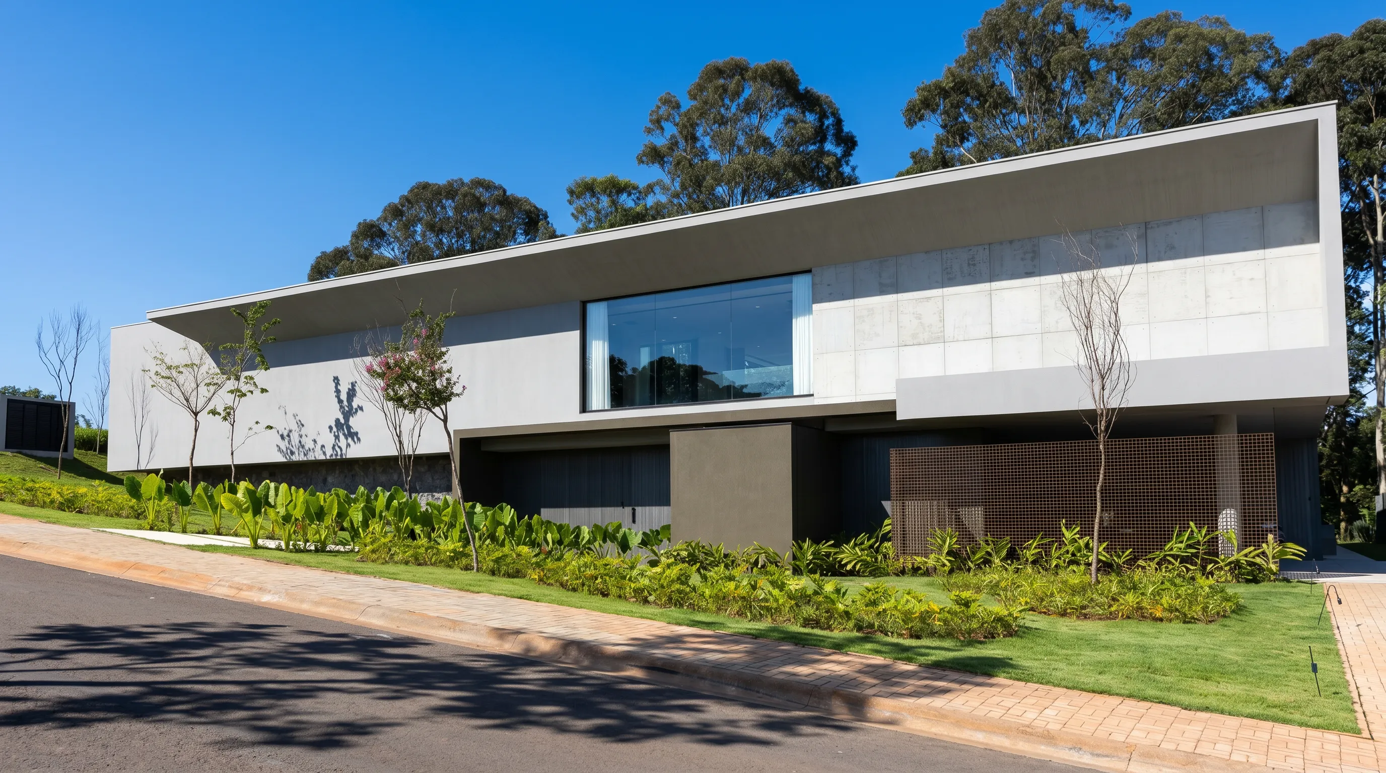 Fachada frontal da Casa Entreverdes na Fazenda da Grama com volume superior em concreto, jardim sobre talude e bosque preservado ao fundo