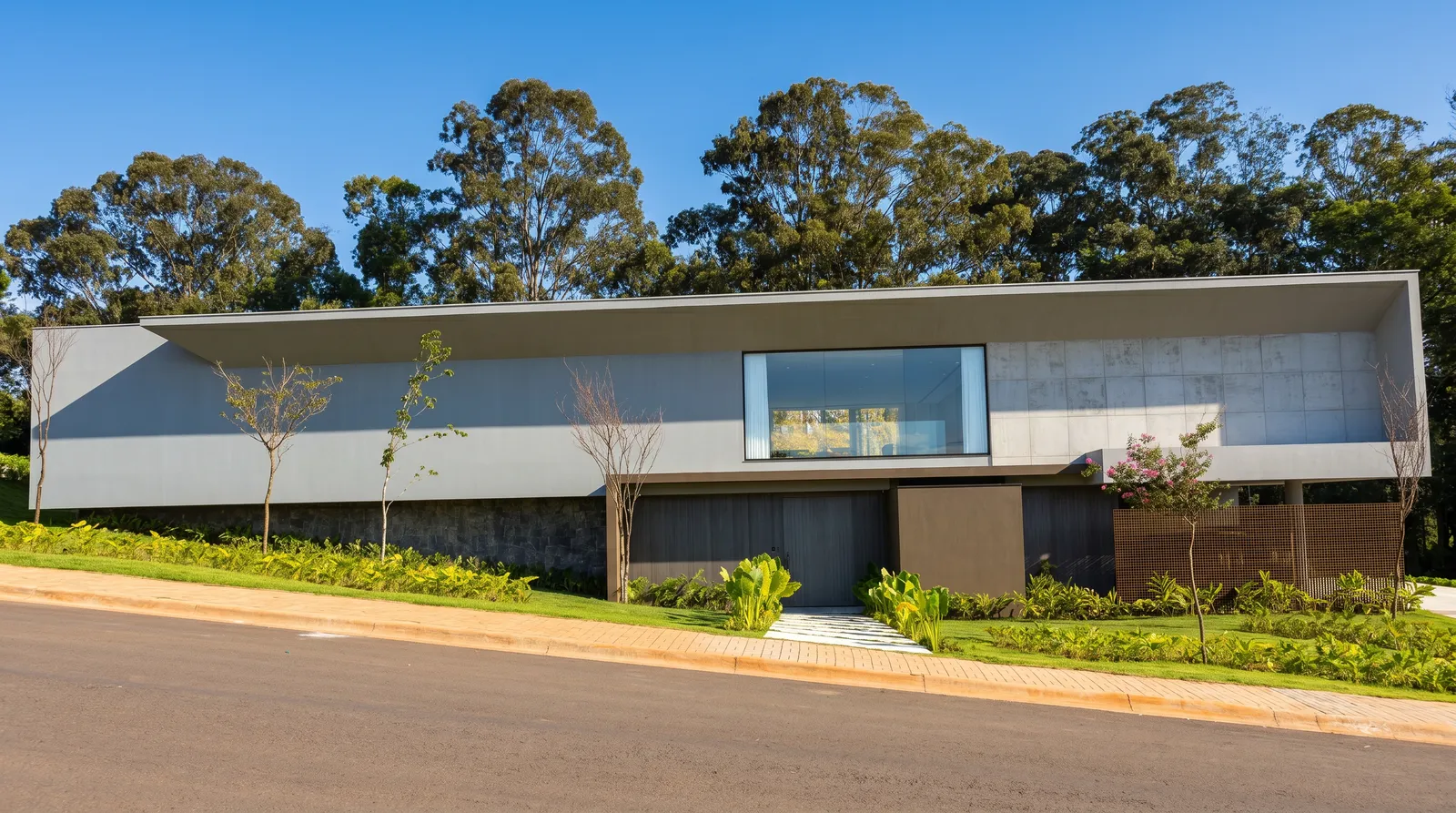 Fachada horizontal da Casa Entreverdes na Fazenda da Grama, residência de alto padrão em alvenaria com bosque ao fundo, taludes laterais e paisagismo integrado