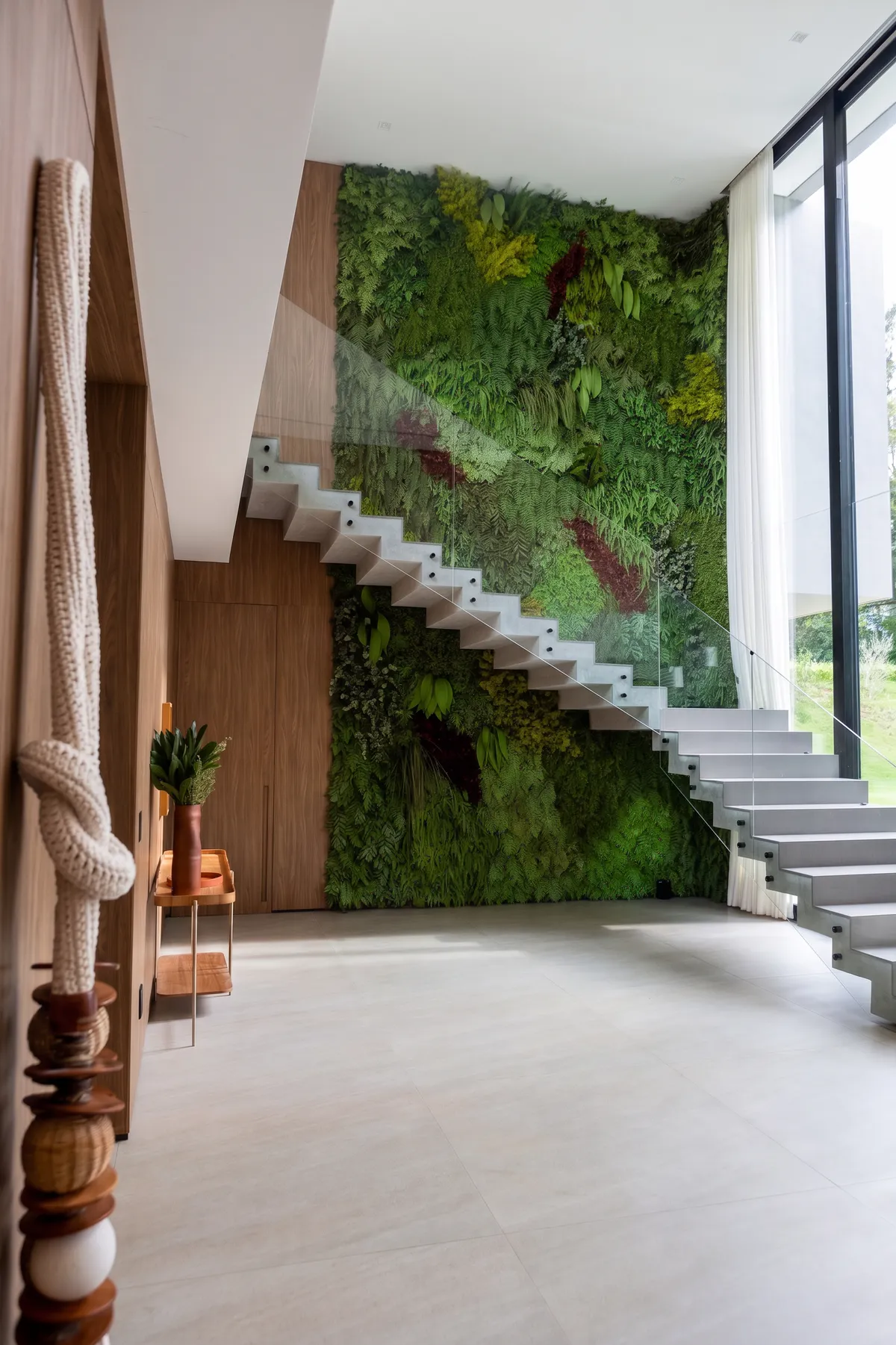 Escada interna da Casa Entreverdes na Fazenda da Grama com jardim vertical, degraus claros, guarda-corpo de vidro e pé-direito duplo