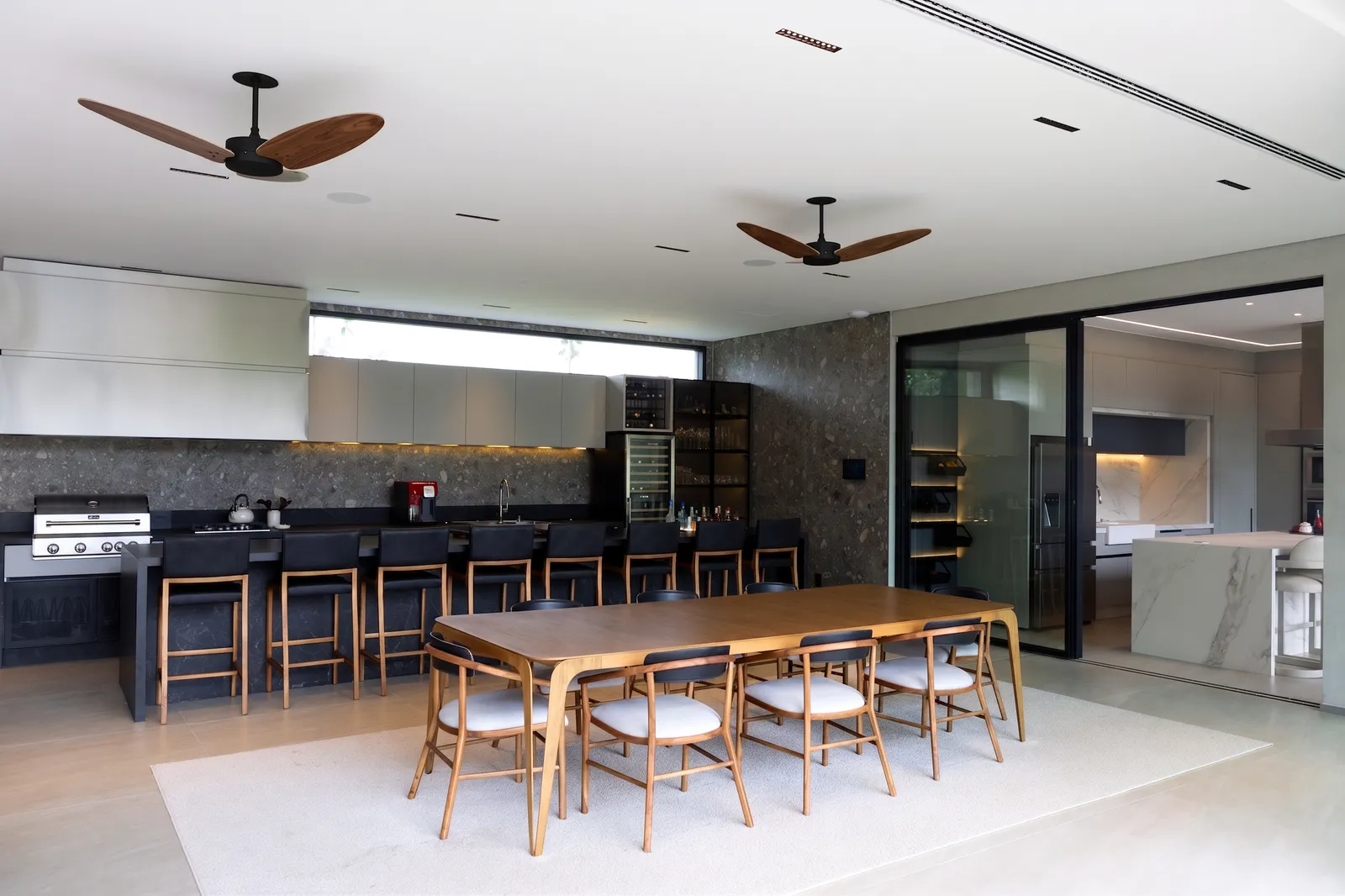 Gourmet da Casa Entreverdes com bancada preta, churrasqueira, adega, mesa de jantar em madeira e cozinha integrada ao fundo