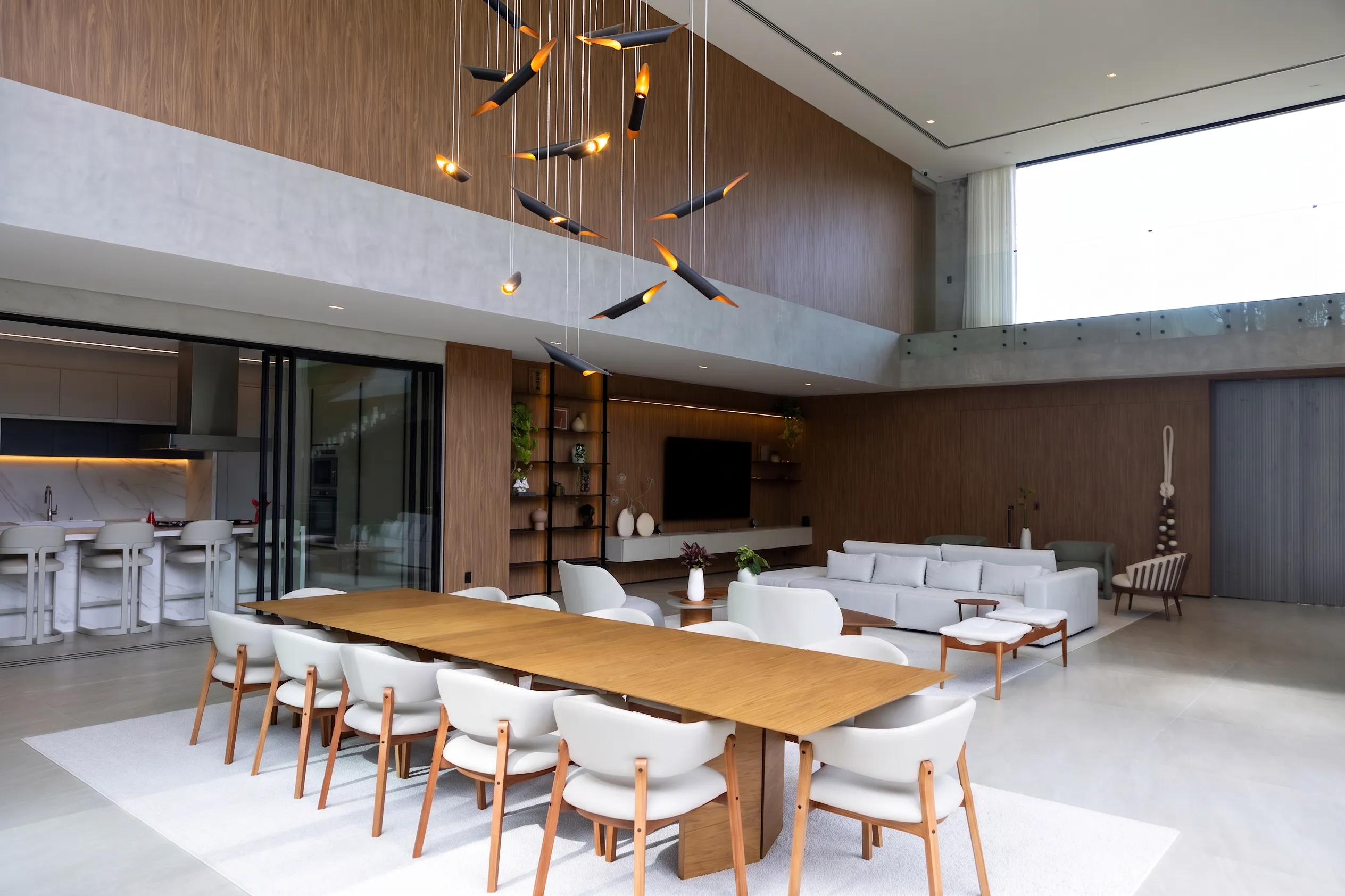 Mesa de jantar da Casa Entreverdes com pendente escultórico, painel de madeira, living integrado e pé-direito duplo