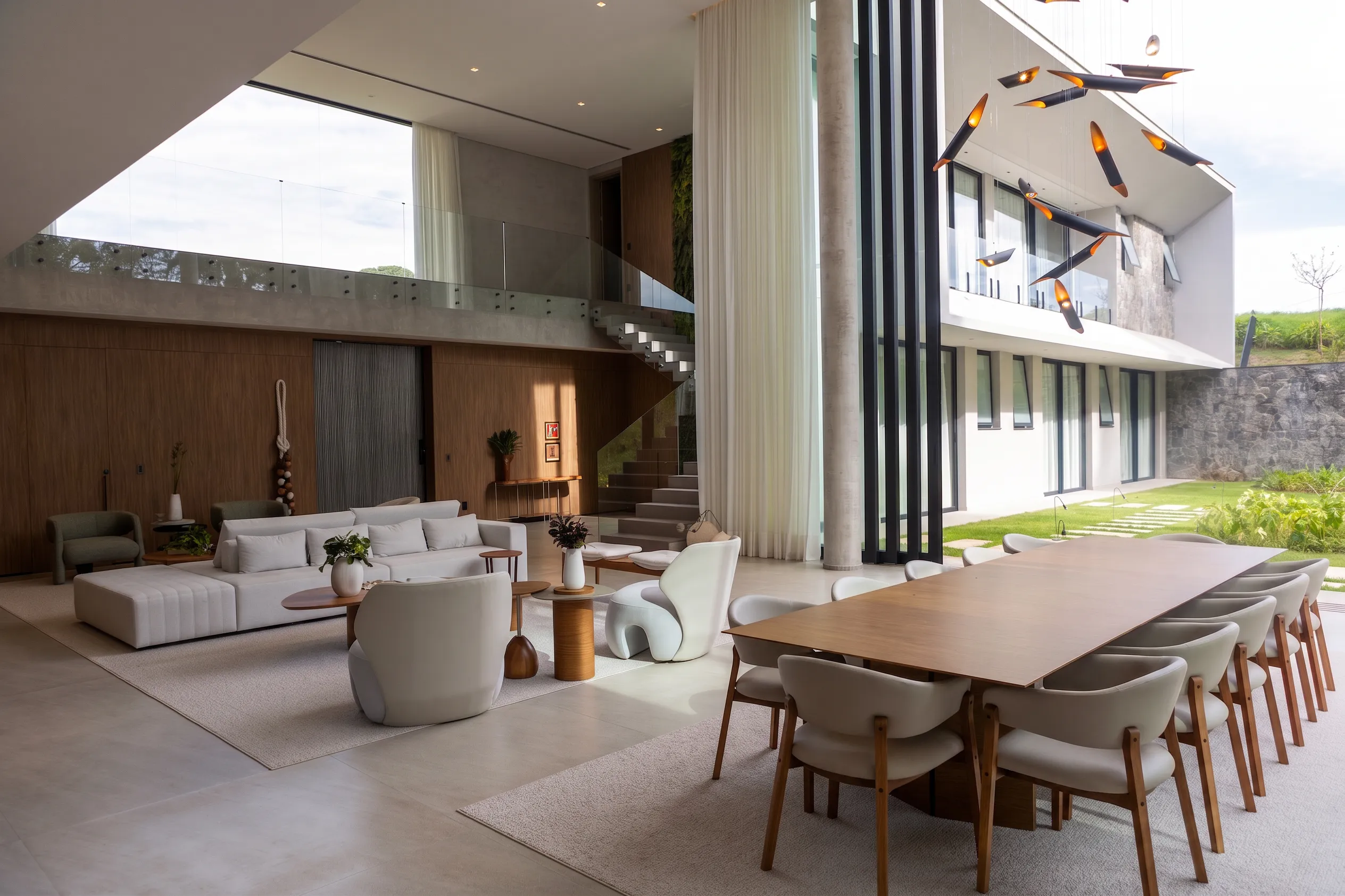 Jantar e varanda de pé-direito duplo da Casa Entreverdes com pendente escultórico, mesa de madeira e vista para piscina
