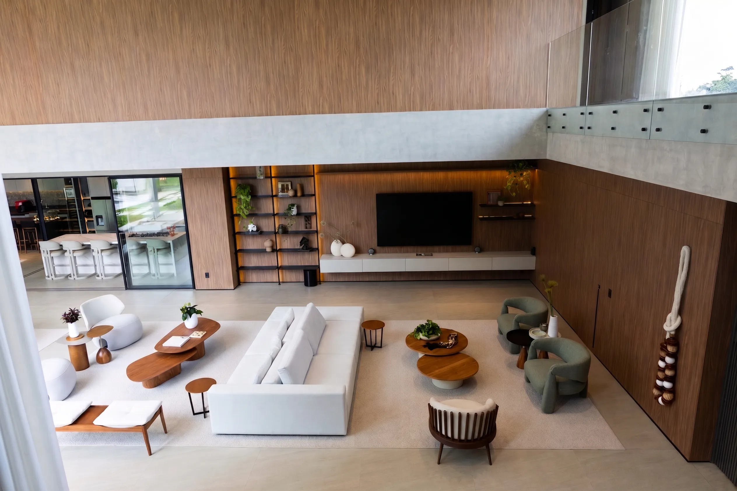 Living de pé-direito duplo da Casa Entreverdes com painel de TV em madeira, sofá modular claro, poltronas verdes e guarda-corpo de vidro