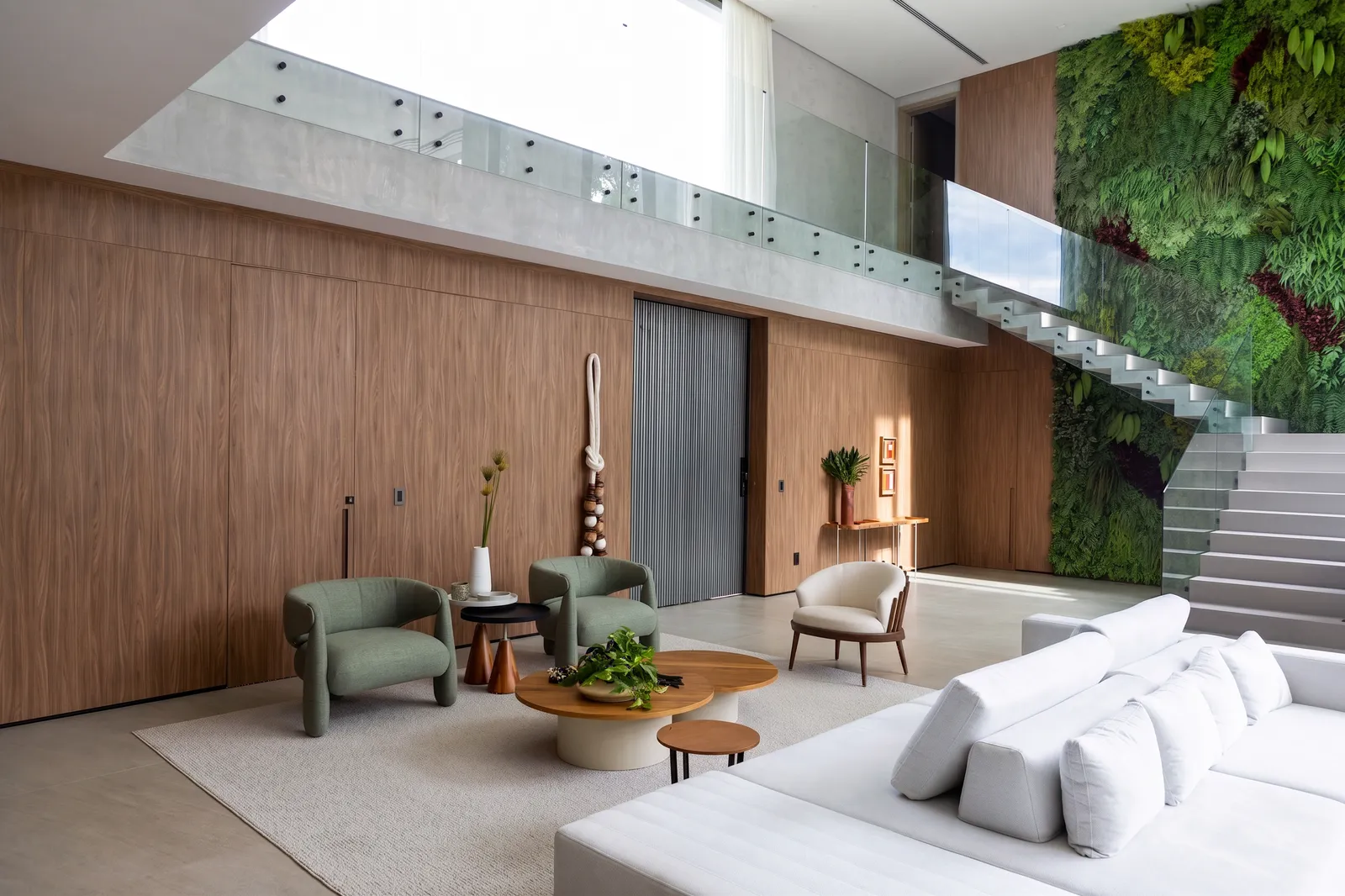 Living da Casa Entreverdes com escada, jardim vertical, painel de madeira, sofá claro, poltronas verdes e pé-direito duplo