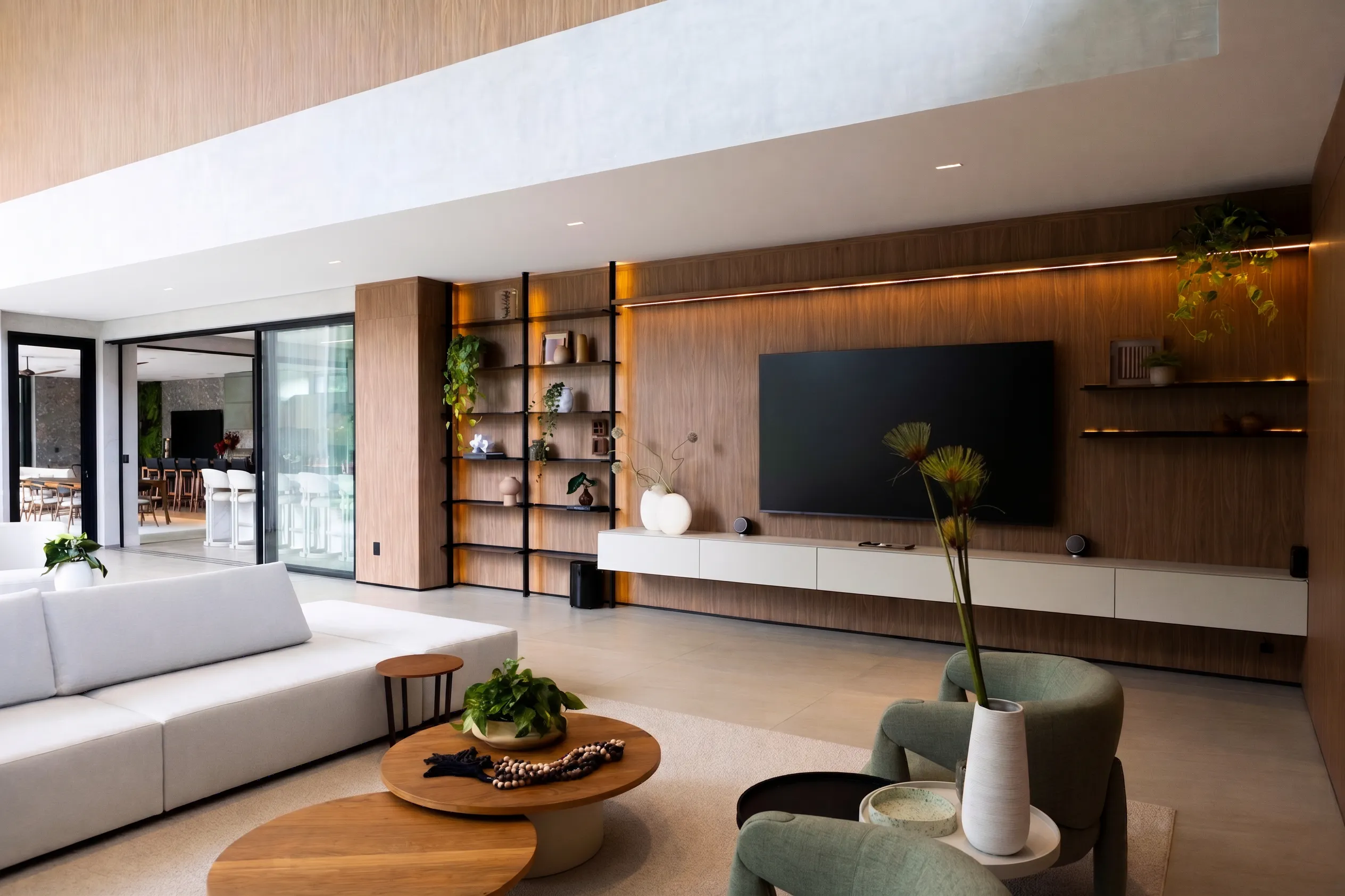 Living da Casa Entreverdes com painel de madeira, estantes metálicas, sofá claro, poltronas verdes e integração visual com o gourmet