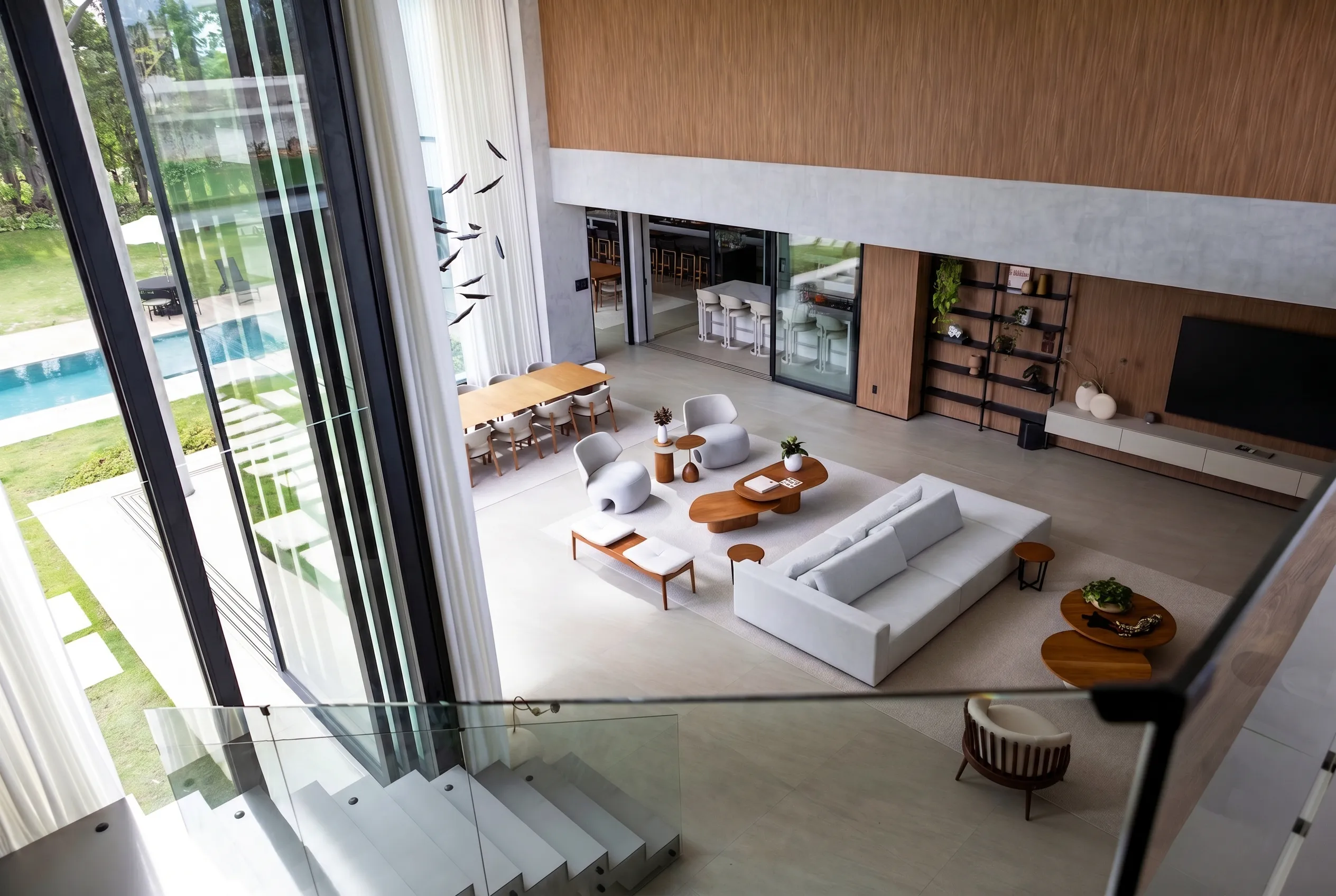 Mezanino sobre o living da Casa Entreverdes com guarda-corpo de vidro, pé-direito duplo, painel de madeira e vista para a piscina