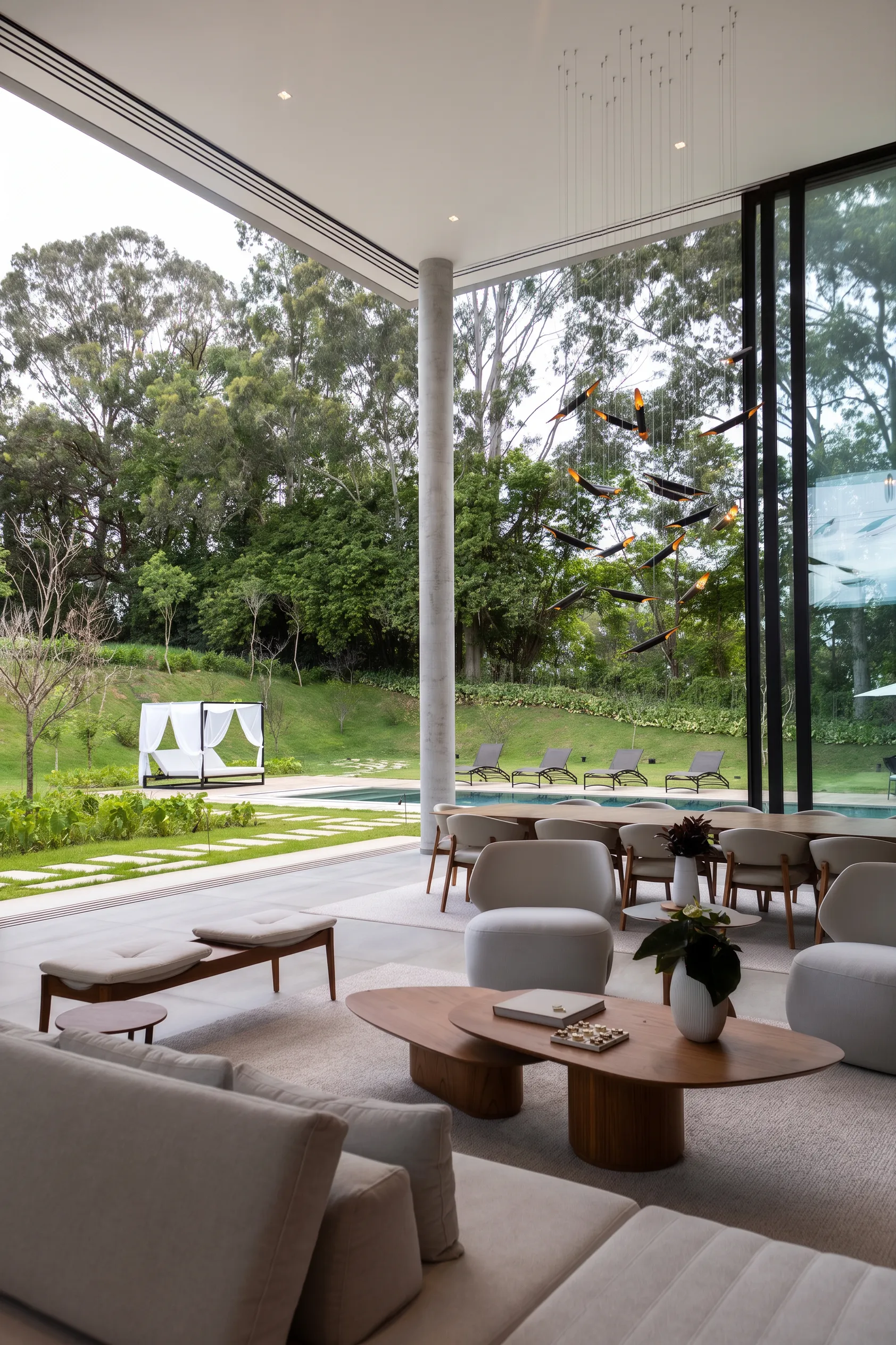Sala de estar da Casa Entreverdes voltada para piscina e bosque, com sofá claro, poltronas orgânicas e cortinas de pé-direito duplo