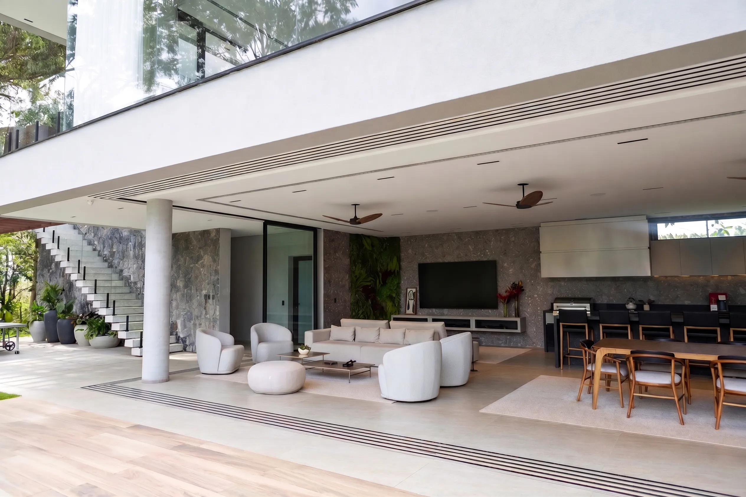 Varanda gourmet da Casa Entreverdes com estar, bancada em pedra escura, parede mineral, escada lateral e abertura total para o jardim