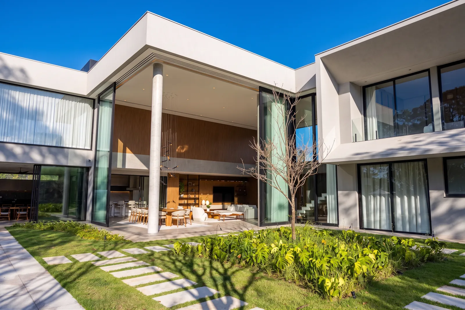 Living integrado da Casa Entreverdes aberto para o jardim, com grandes panos de vidro, pé-direito duplo e área gourmet conectada à piscina
