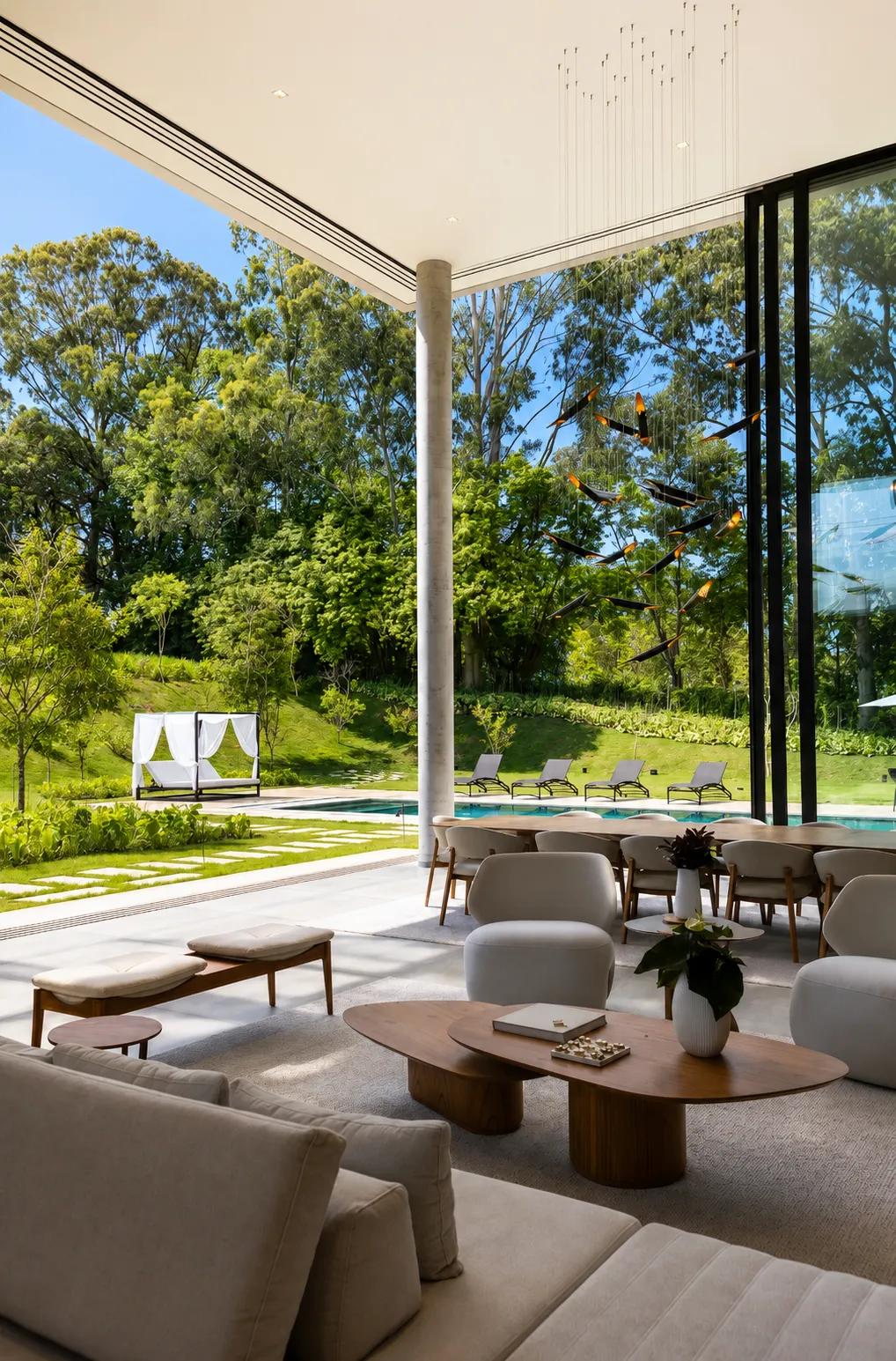 Living da Casa Entreverdes com pé-direito duplo aberto para piscina, bosque, talude verde e área de estar integrada
