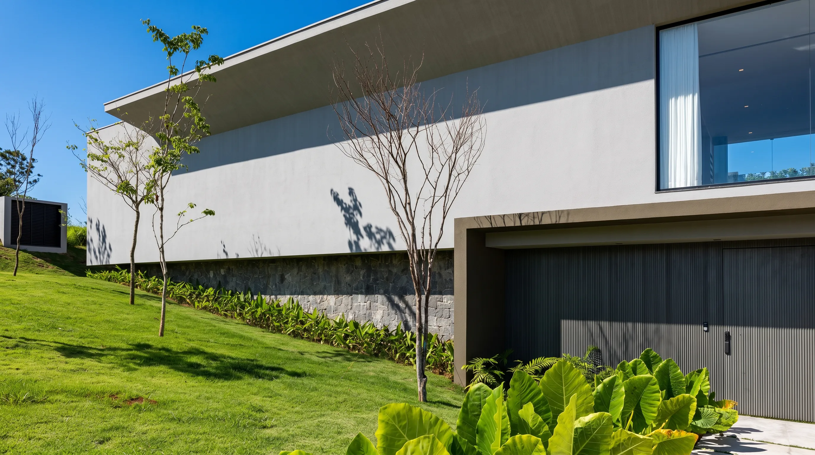 Volume superior da Casa Entreverdes na Fazenda da Grama com jardim frontal, fachada em alvenaria e relação com o bosque
