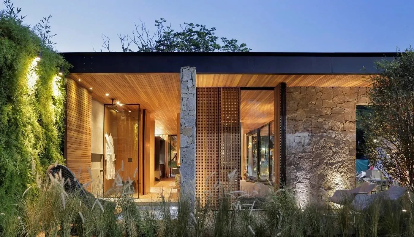 Residência térrea contemporânea com estrutura metálica, vidro, pedra, madeira e jardim iluminado.