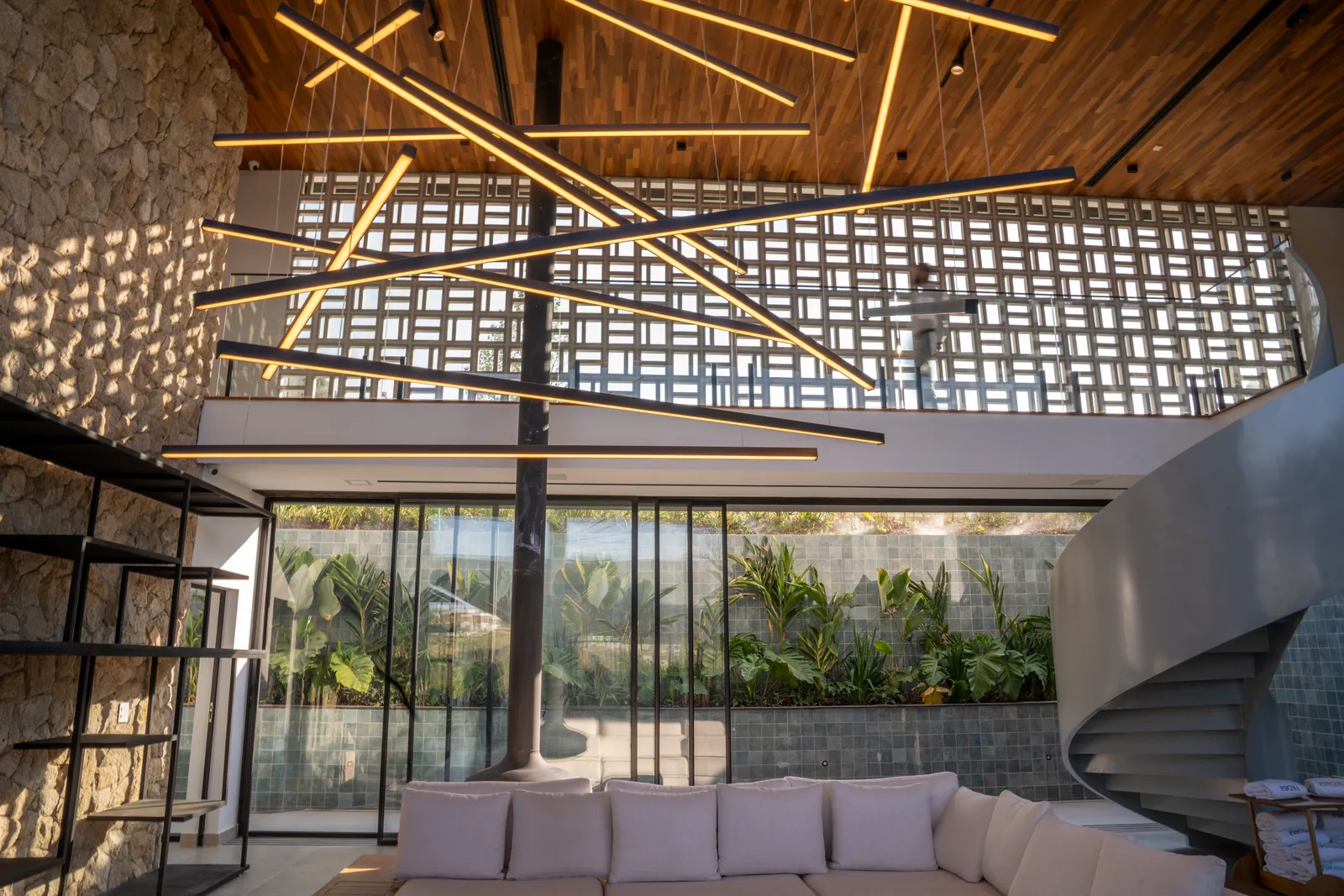 Interior da Casa Hof com pé-direito duplo, pedra natural, lareira suspensa, escada helicoidal e iluminação linear