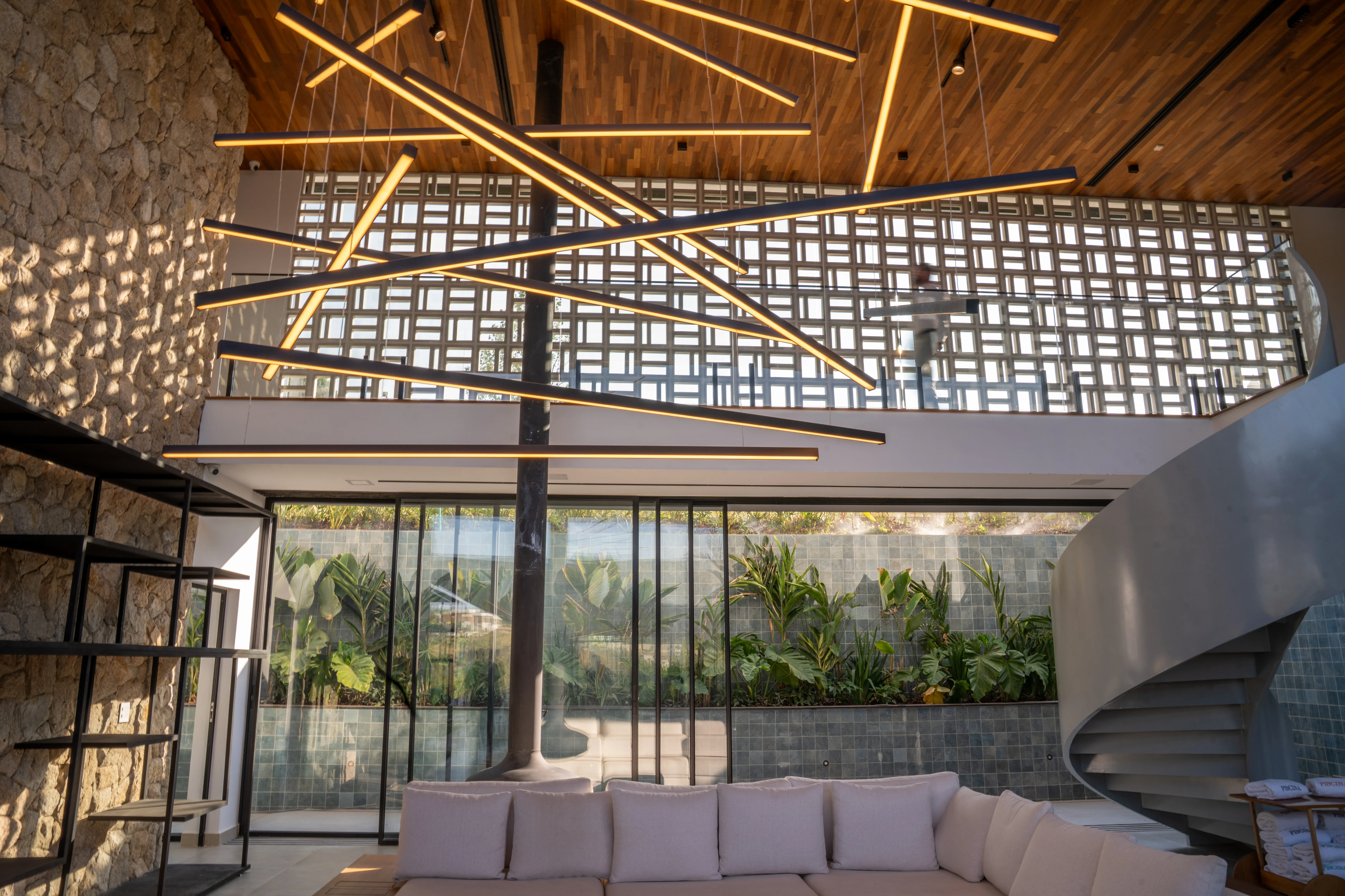 Interior da Casa Hof com pé-direito duplo, pedra natural, forro de madeira, aço e iluminação linear