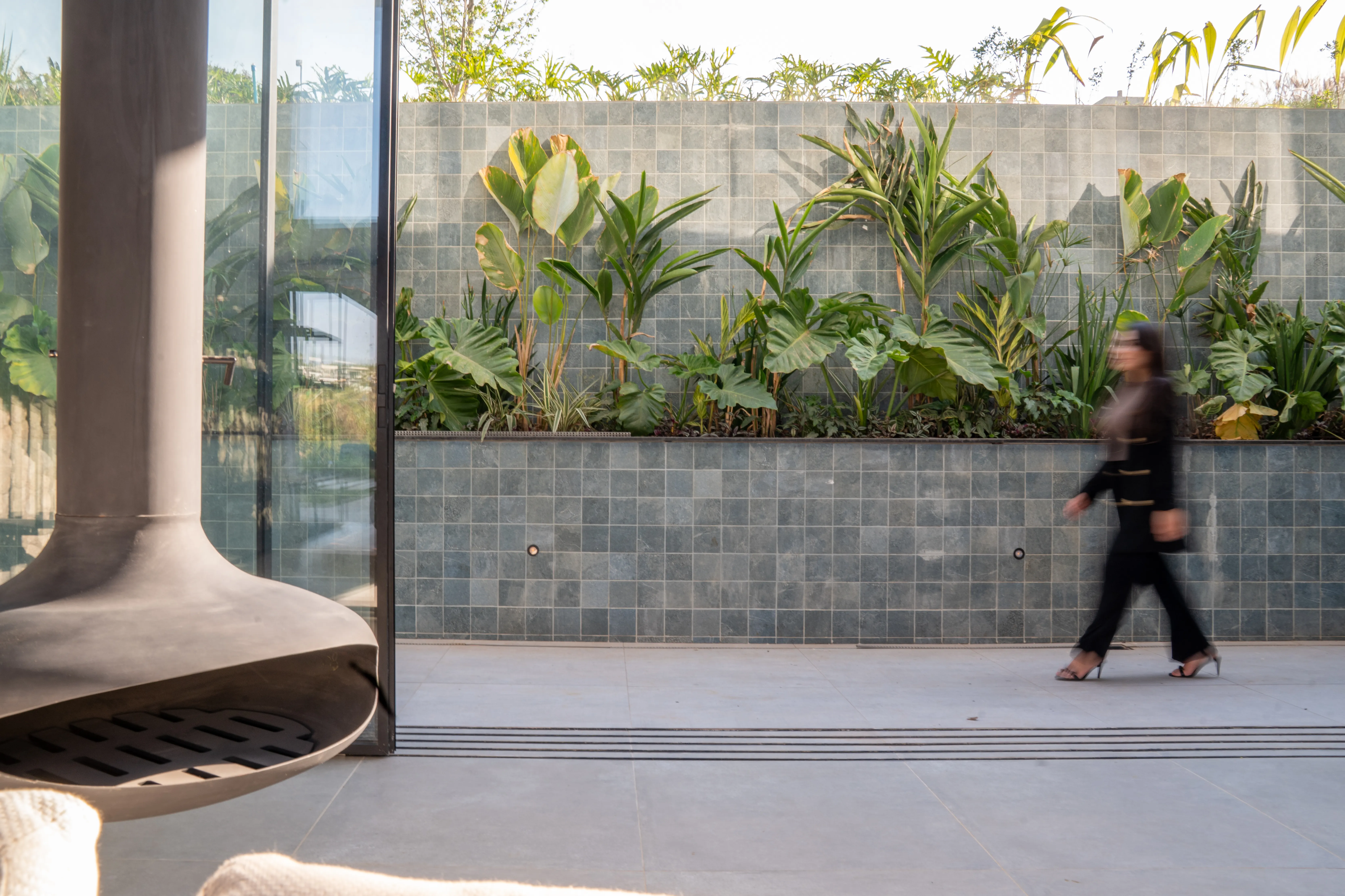 Jardim interno da Casa Hof com vegetação tropical, lareira suspensa e grandes aberturas de vidro