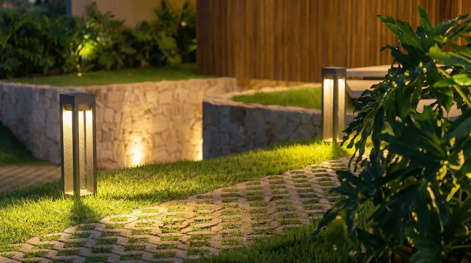Caminho de acesso da Casa Trama com piso drenante, balizadores de luz, muros de pedra natural e vegetação tropical