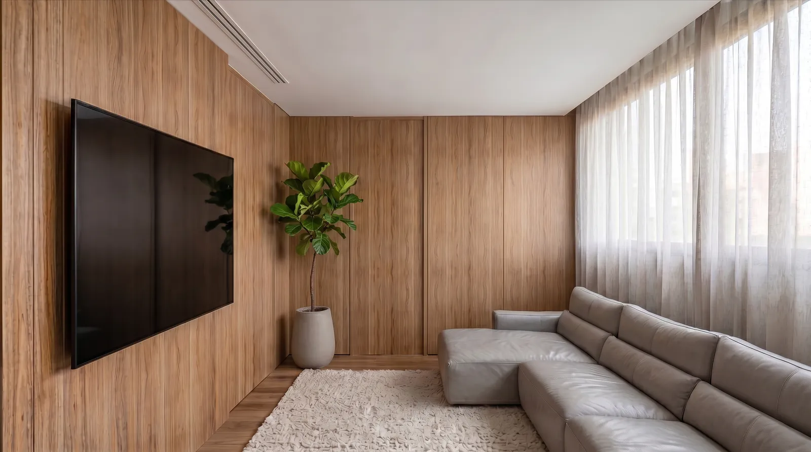 Sala íntima da Casa Trama em Alphaville Campinas com paredes em madeira, sofá cinza, cortinas translúcidas, tapete claro e planta junto ao painel