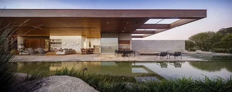 Residência contemporânea com estrutura metálica aparente, pano de vidro, piscina e forro ripado de madeira.